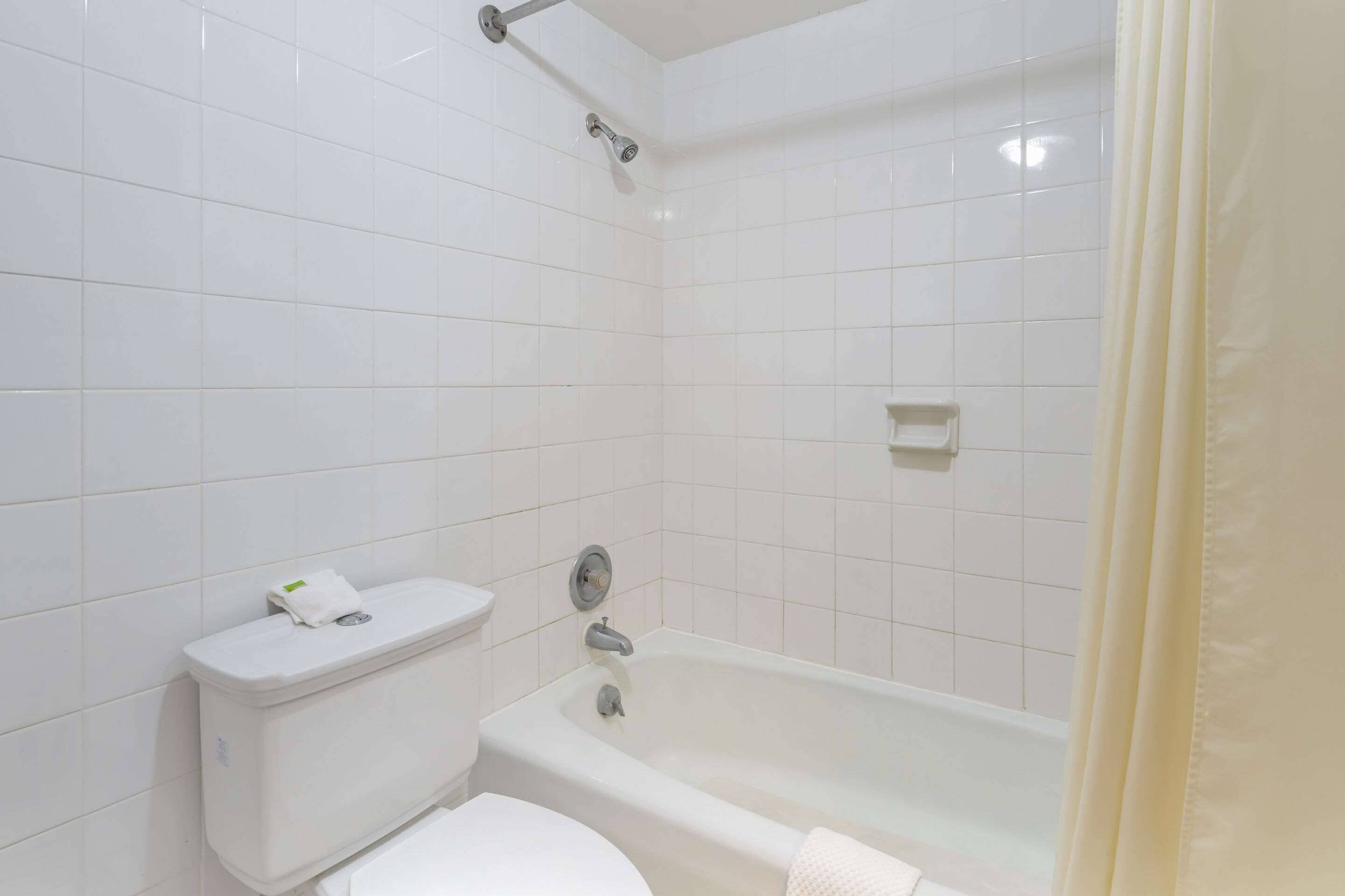 Ein Badezimmer mit weißen Fliesen, einer Toilette, einer Badewanne und einem Duschkopf.
