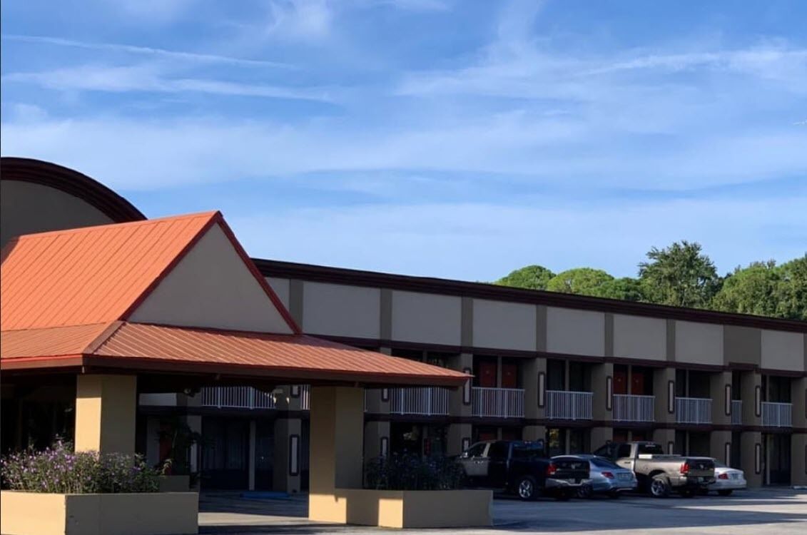 Un motel con techo rojo, varios balcones y un estacionamiento con algunos coches.