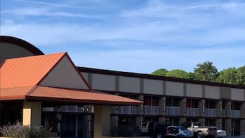 Un motel con techo rojo, varios balcones y un estacionamiento con algunos coches.