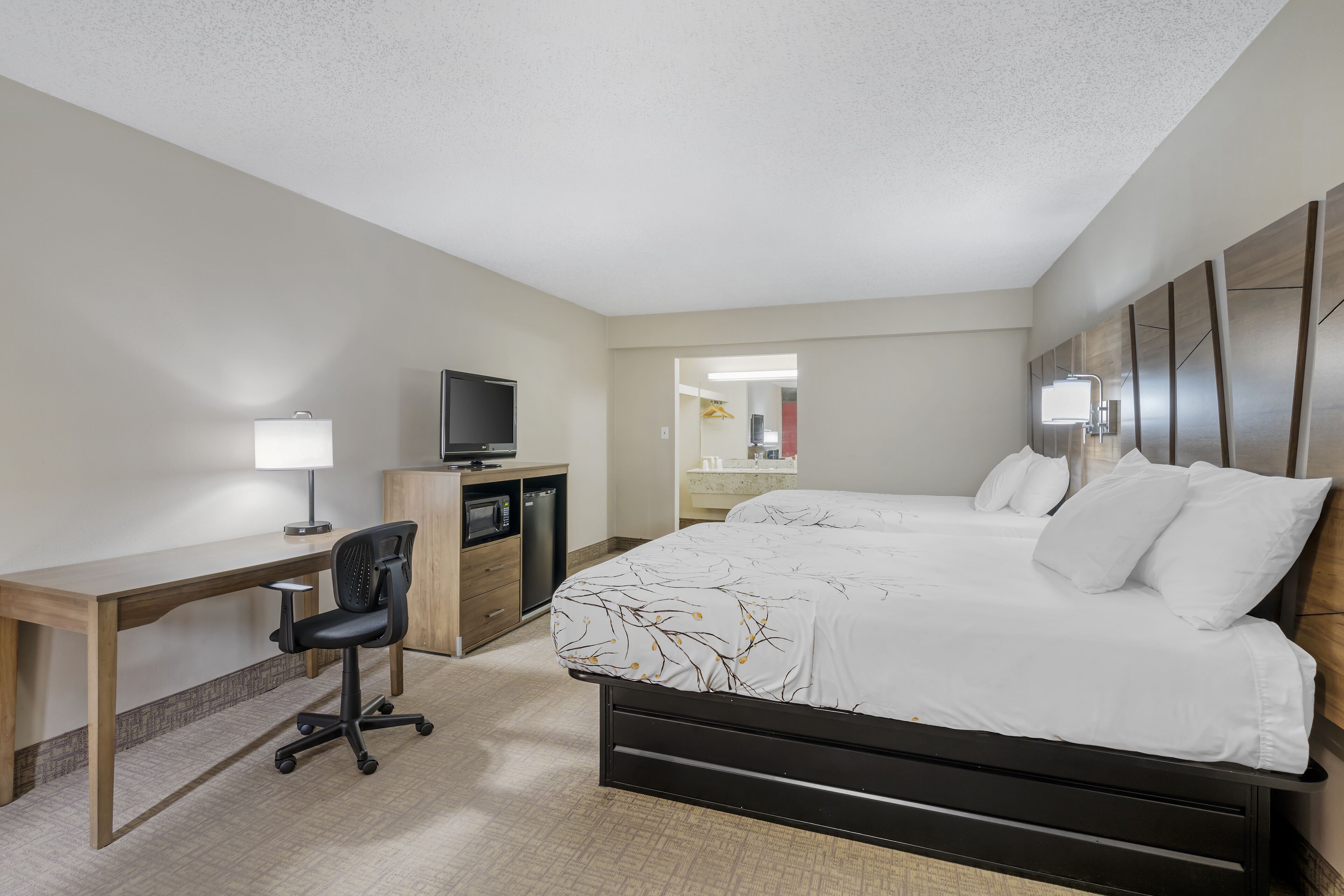 A hotel room with a bed, desk, chair, TV, and a bathroom visible through an open door.