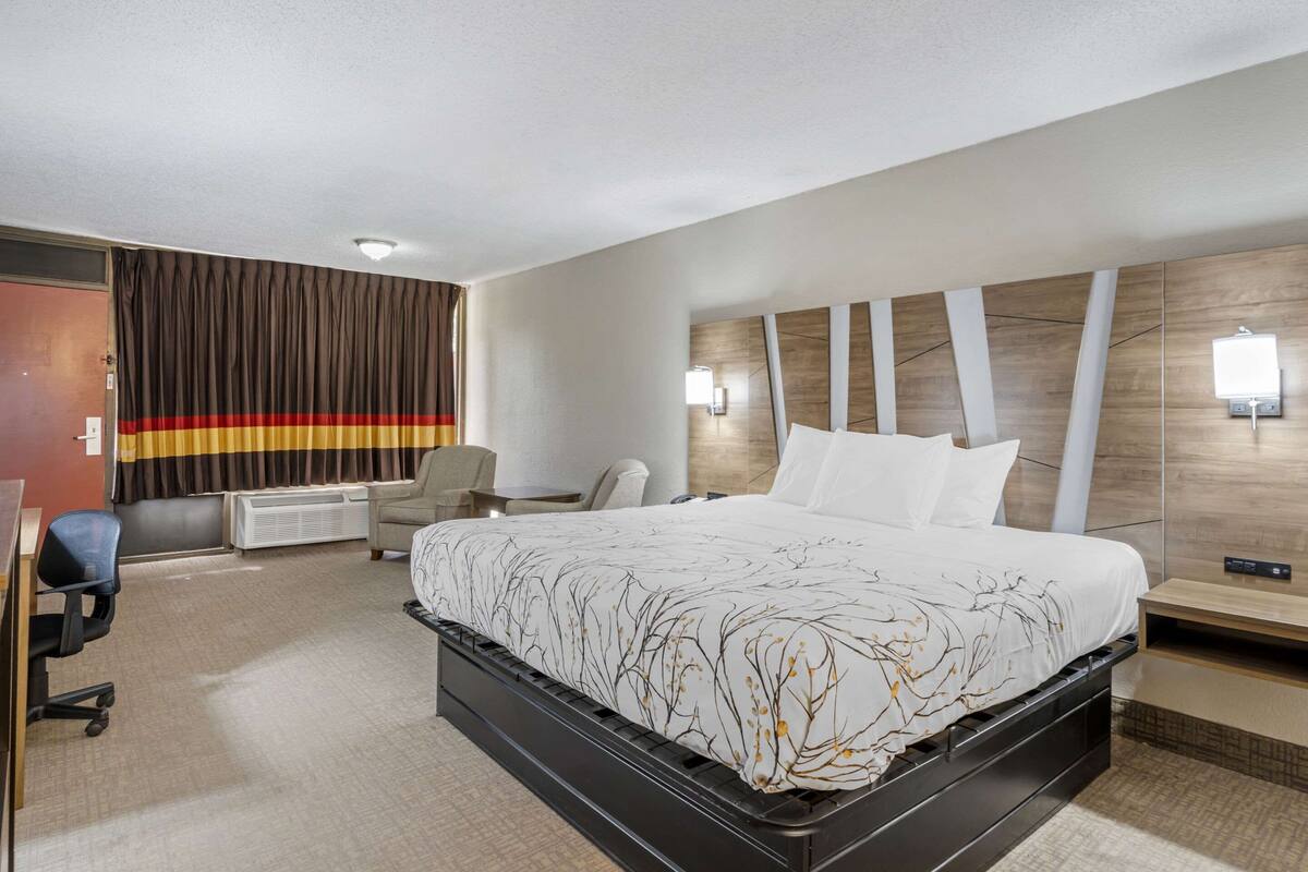 A hotel room with a large bed, a desk, a chair, and a wall-mounted TV.