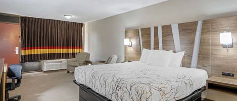A hotel room with a large bed, a desk, a chair, and a wall-mounted TV.