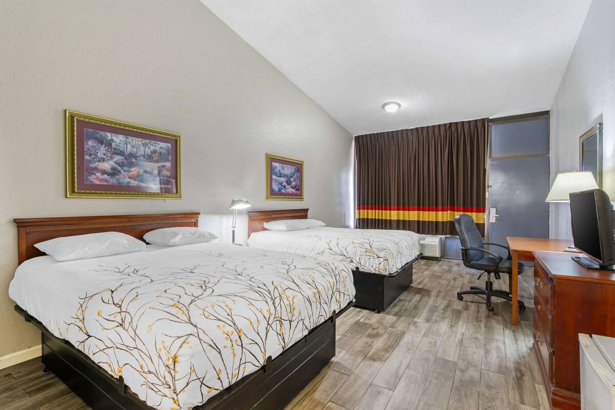 A hotel room with two beds, a desk with a chair, a TV, and two framed pictures on the wall.