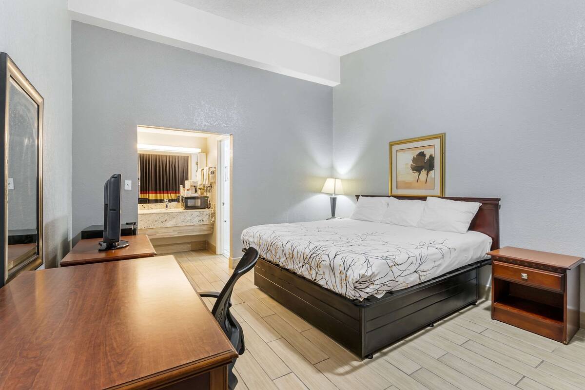 A hotel room with a bed, bedside table, desk, chair, and a bathroom visible through an open door.