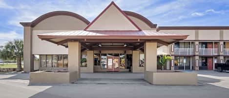 A hotel entrance with a covered walkway, large windows, and a parking area.