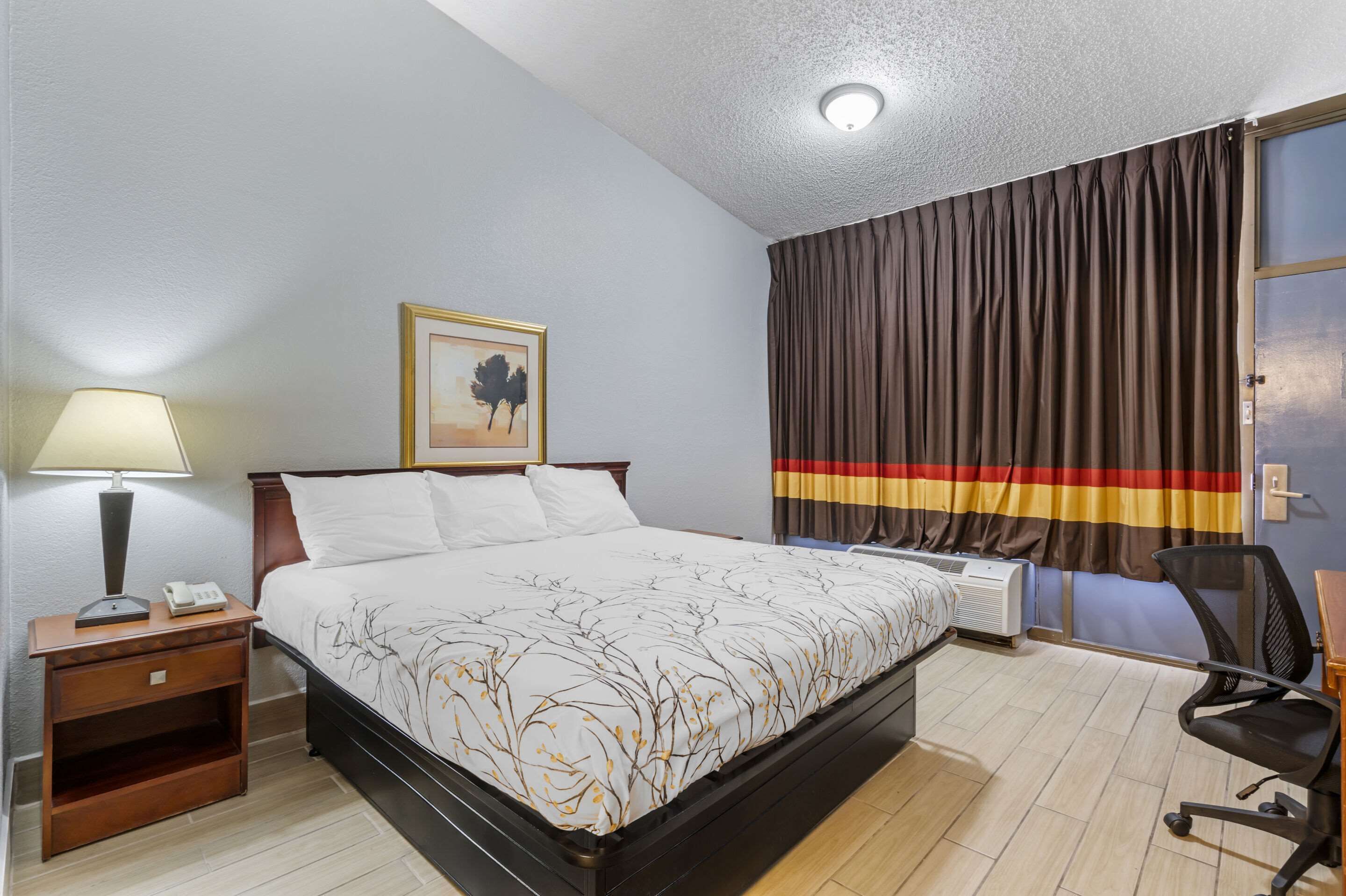 A hotel room with a bed, a nightstand with a lamp, a chair, and a window with curtains.