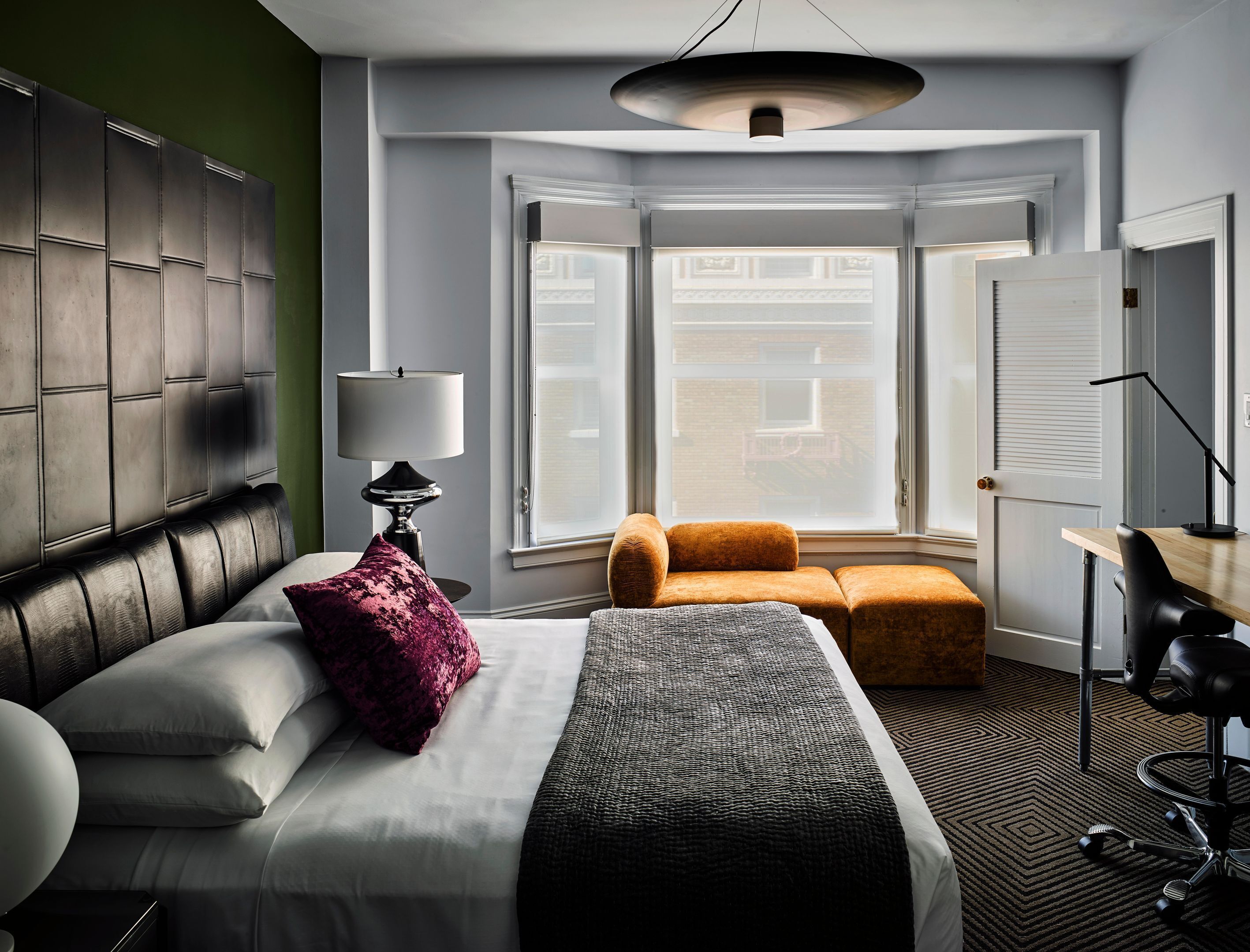 Ein Hotelzimmer mit Bett, Schreibtisch, Stuhl, Fenster mit Blick und Lampe.