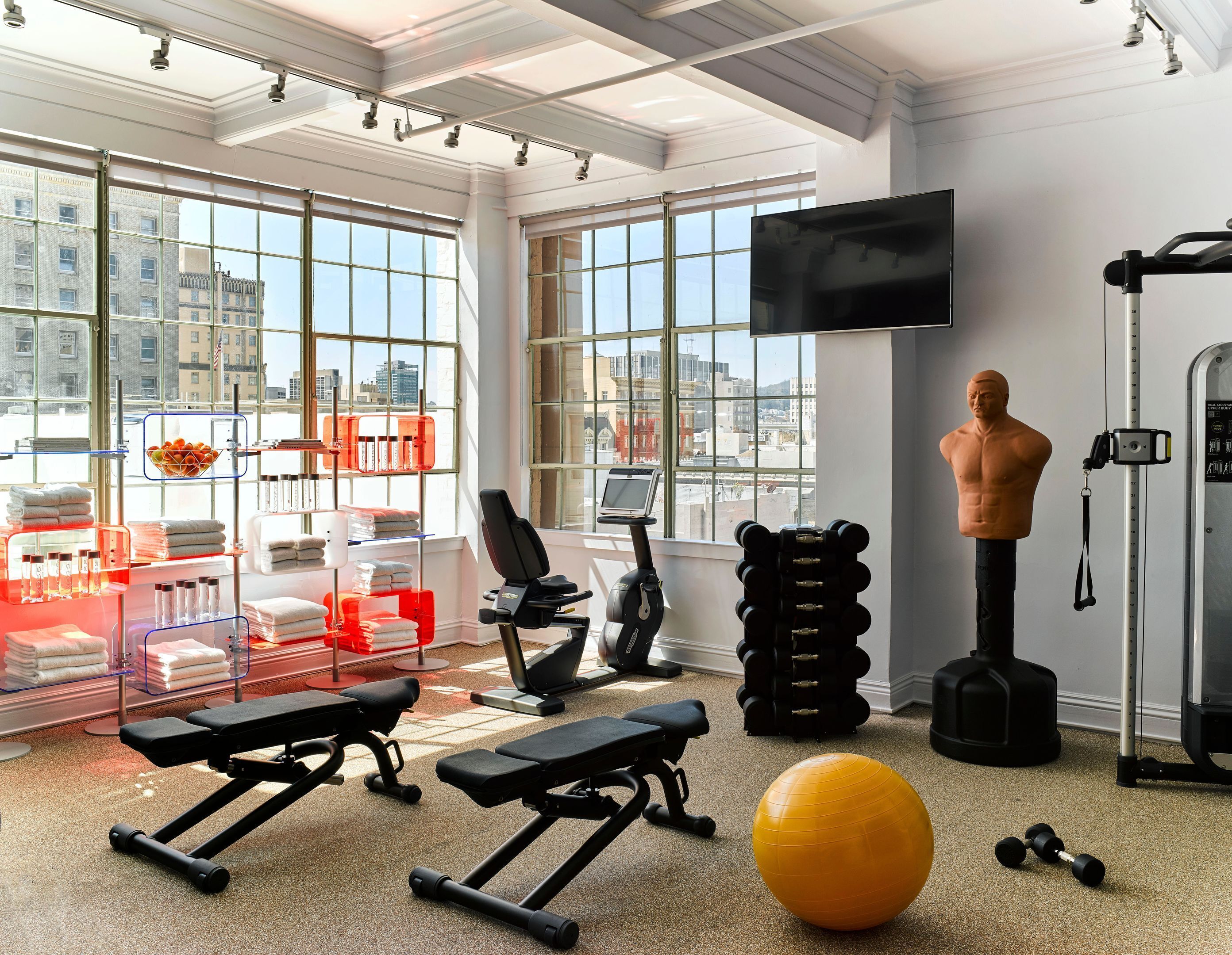 Et fitnesscenter med træningsudstyr, et stort vindue og udsigt over byen.