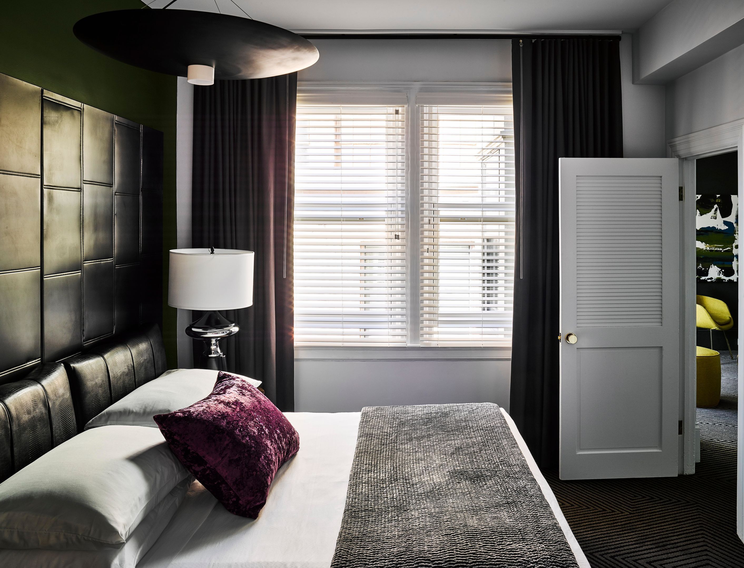 Una habitación de hotel con una cama, una lámpara, una ventana con persianas y una puerta.