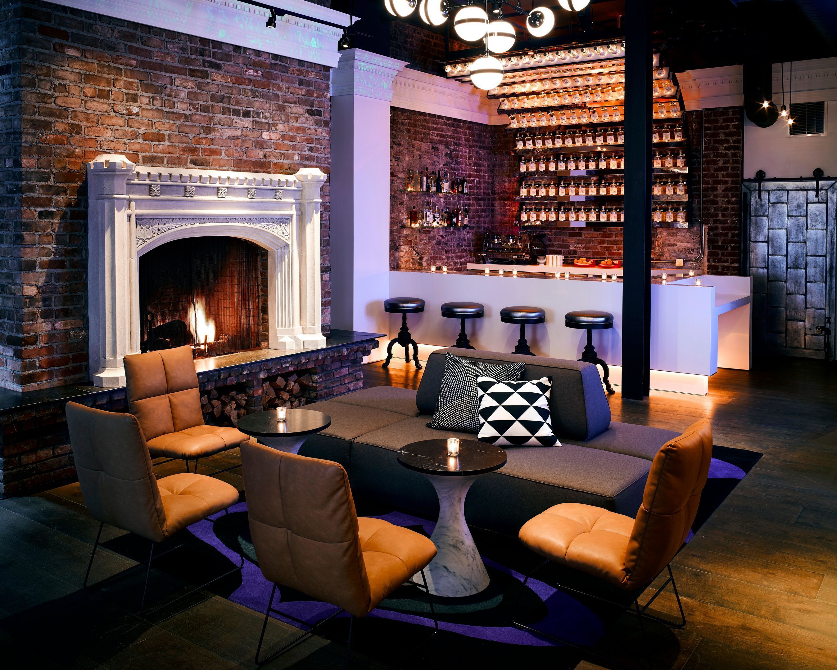 A bar area with a brick wall, a fireplace, bar stools, and a seating area with chairs and a table.