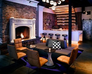 A bar area with a brick wall, a fireplace, bar stools, and a seating area with chairs and a table. - Hotel Zeppelin San Francisco (San Francisco)