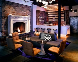 A bar area with a brick wall, a fireplace, bar stools, and a seating area with chairs and a table.