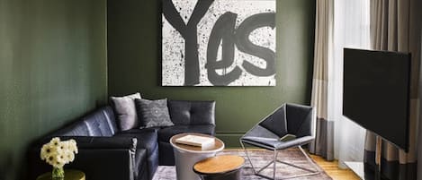 A modern living room with a black leather sofa, a coffee table, and a large TV.