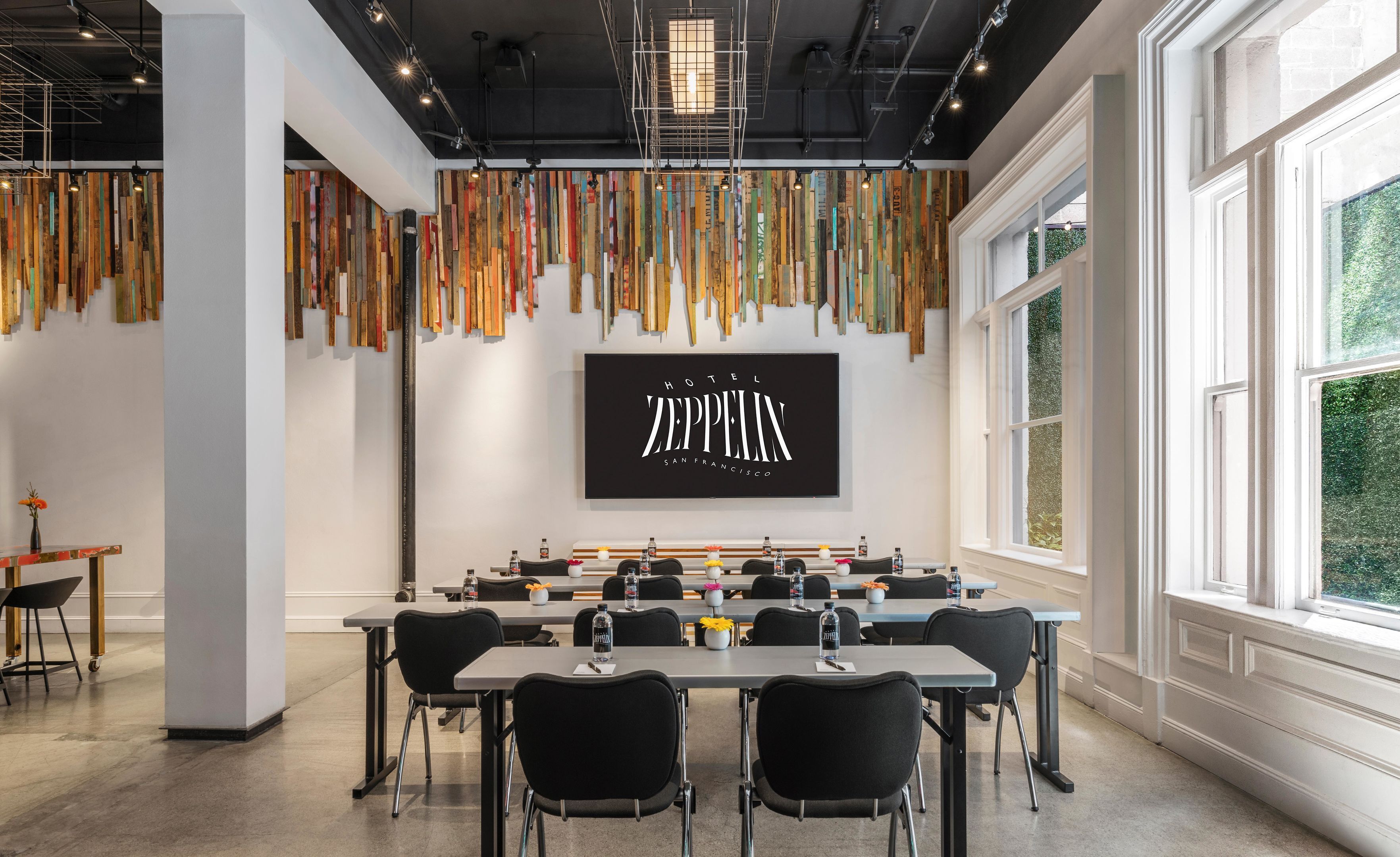 Een vergaderruimte met een lange tafel, zwarte stoelen en een groot scherm waarop 'Hotel Zeppelin San Francisco' staat.
