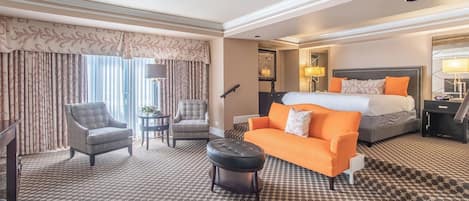 Una habitación de hotel con cama, dos sillones, un sofá, una mesita y una alfombra estampada.