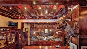 A bar with wooden furniture, a mounted moose head, and a television on the wall.