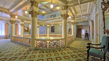Un salón imponente con columnas decorativas, alfombra estampada y un sillón tapizado en verde.