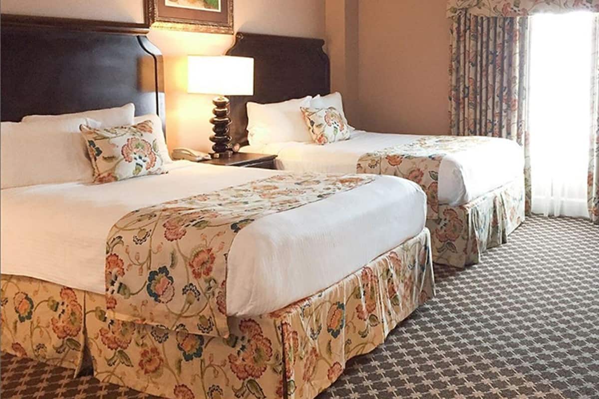 A hotel room with two beds, floral bedspreads, a nightstand with a lamp, and a framed picture on the wall.
