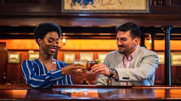 Two people at a bar with wooden furniture and framed artwork on the wall.
