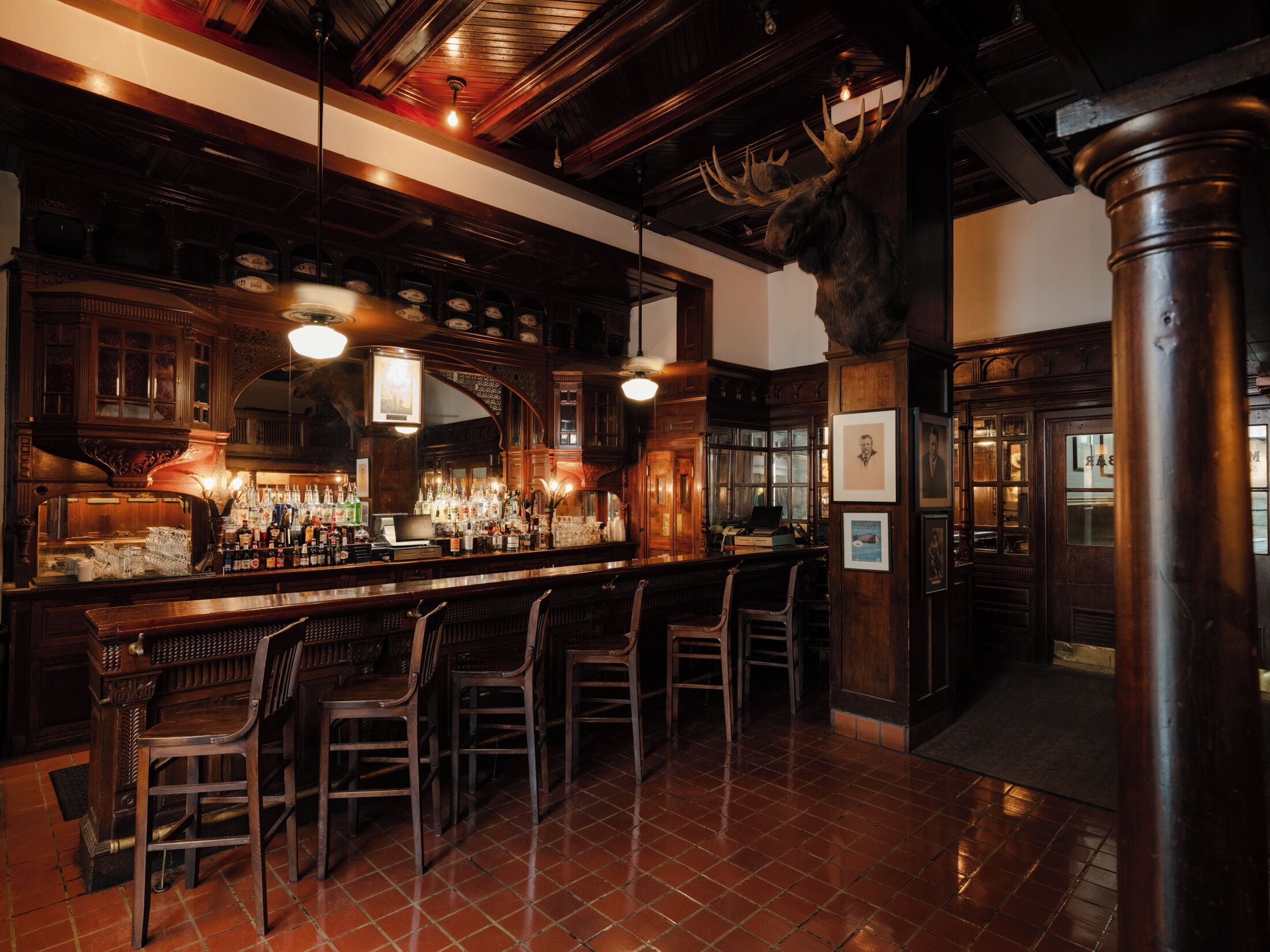 A bar area with wooden bar stools, a counter with bottles, and a mounted moose head.