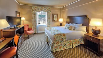 A hotel room with a bed, a desk, a chair, a television, and a window with curtains.