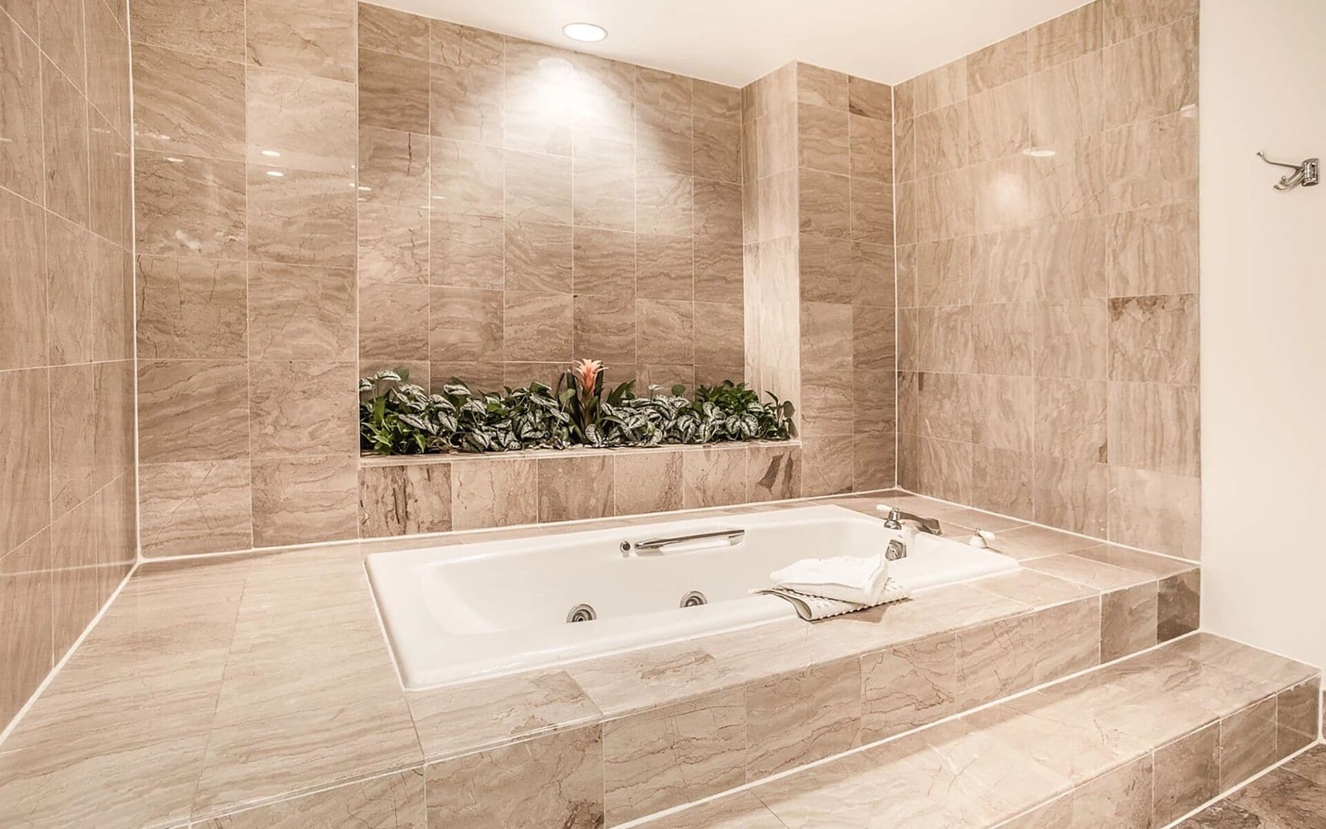 A modern bathroom with a freestanding bathtub, marble walls, and a built-in planter with greenery.