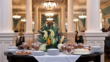 A formal dining setup with a table set for multiple guests, surrounded by white columns and chandeliers.