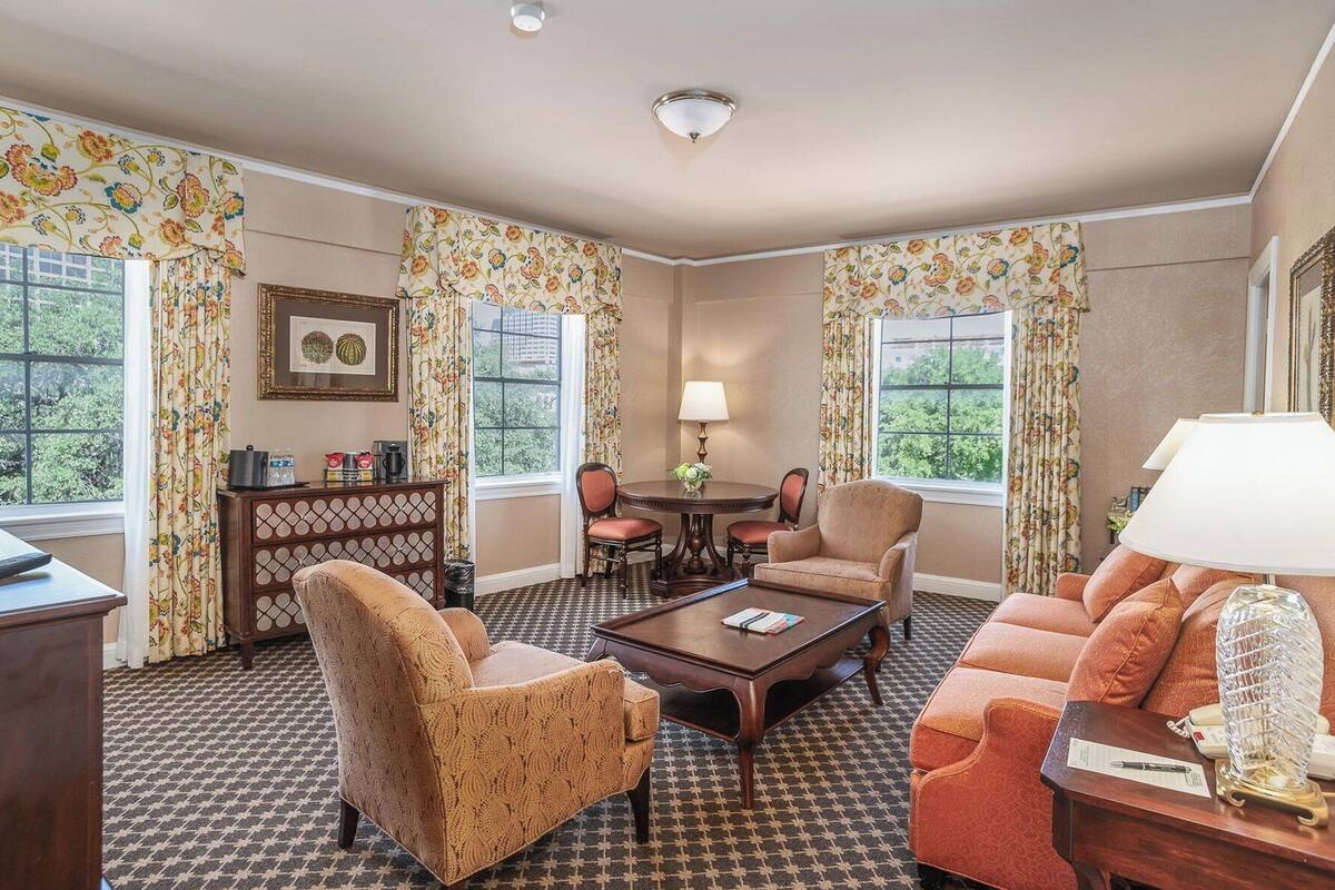 A room with a checkered floor, floral curtains, a dining table with chairs, a sofa, and a lamp.