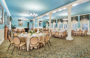 A spacious banquet hall with round tables, chairs, and a patterned carpet.