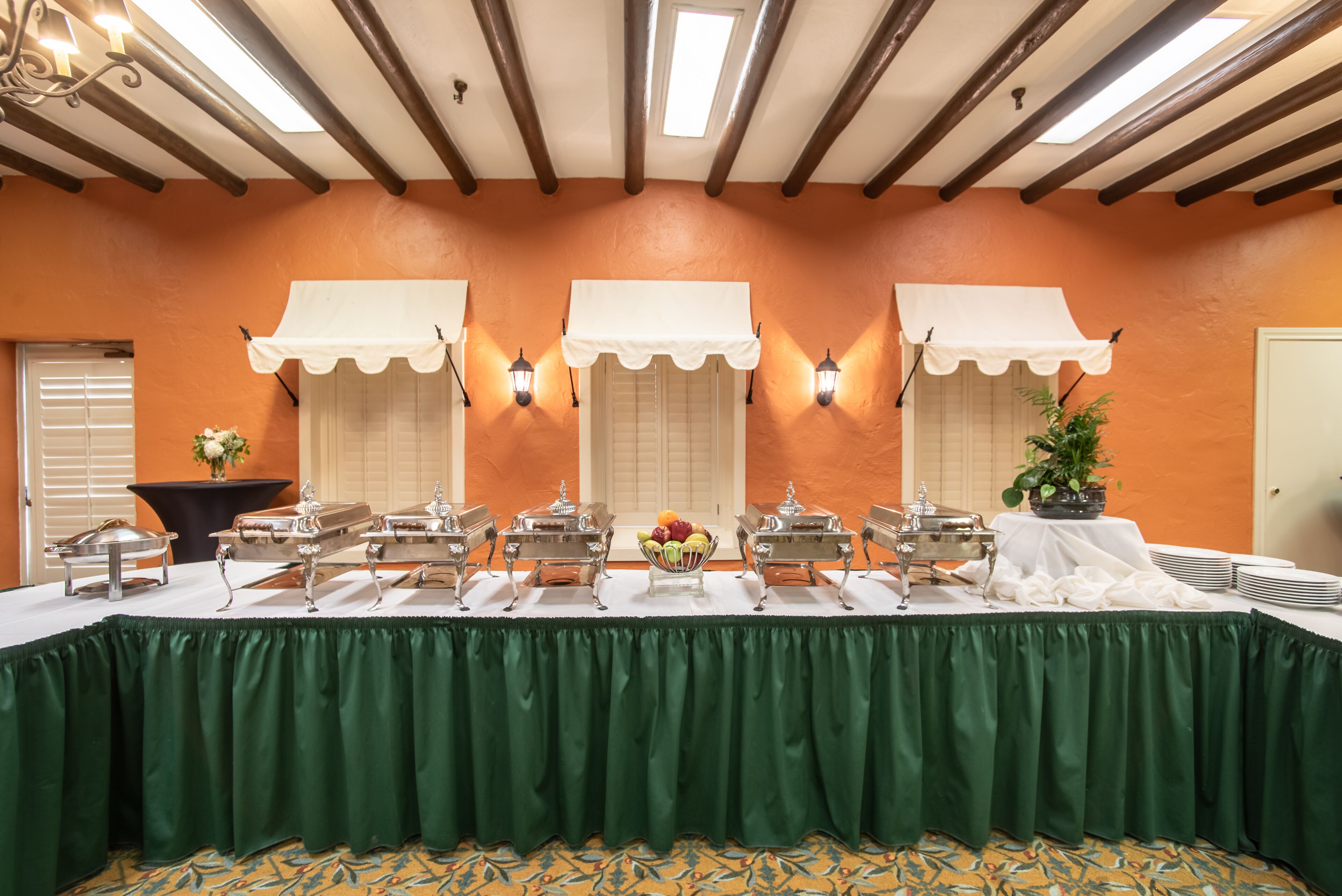 A buffet setup with multiple serving stations, a green tablecloth, and a decorative plant.