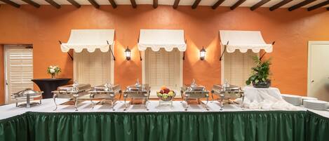 A buffet setup with multiple serving stations, a green tablecloth, and a decorative plant.