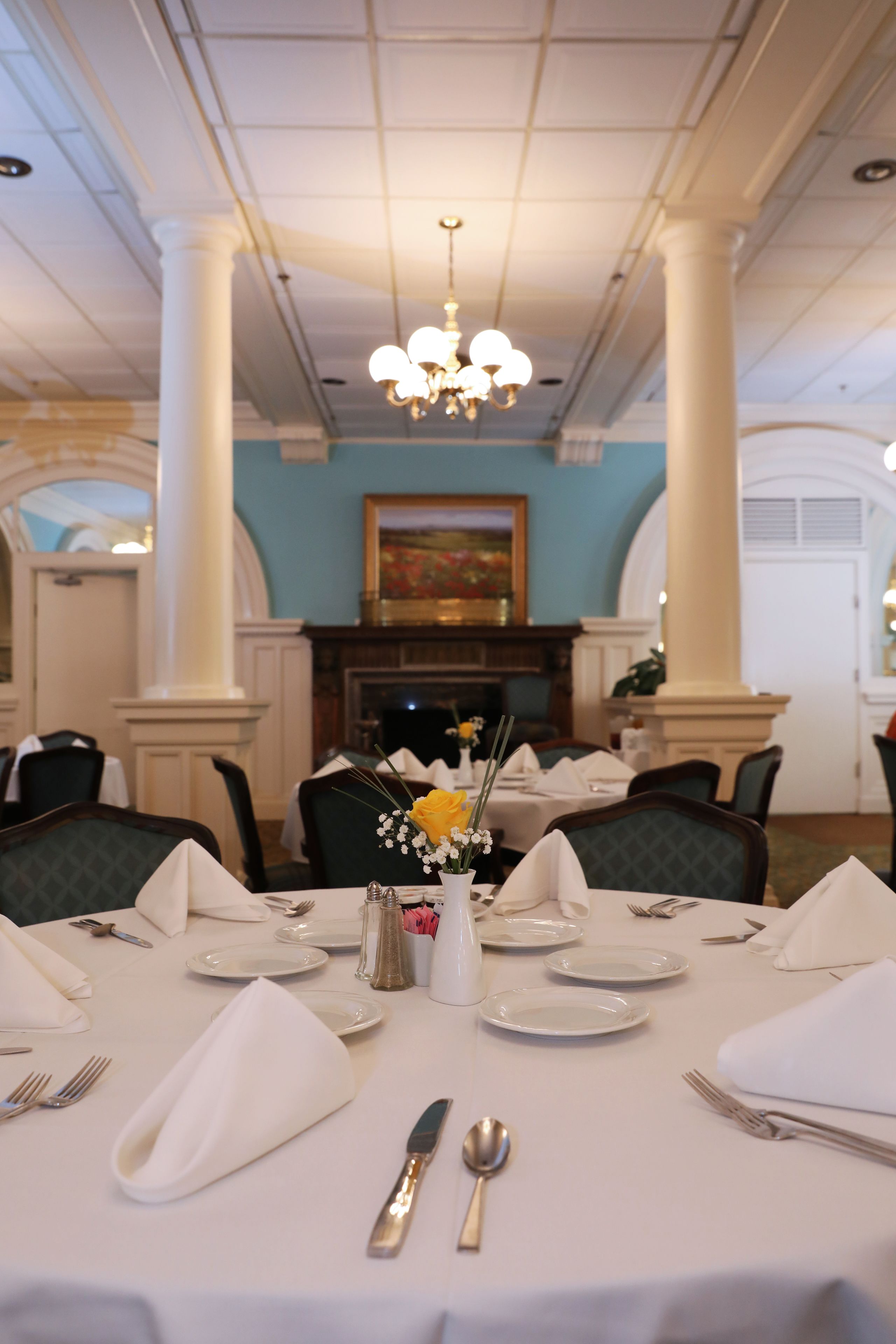 A dining area with tables set for a meal, featuring white tablecloths, silverware, and a vase with flowers.