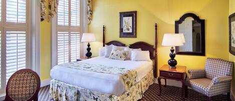 Une chambre d’hôtel avec un grand lit, deux tables de chevet avec des lampes, une chaise et une fenêtre avec des volets.