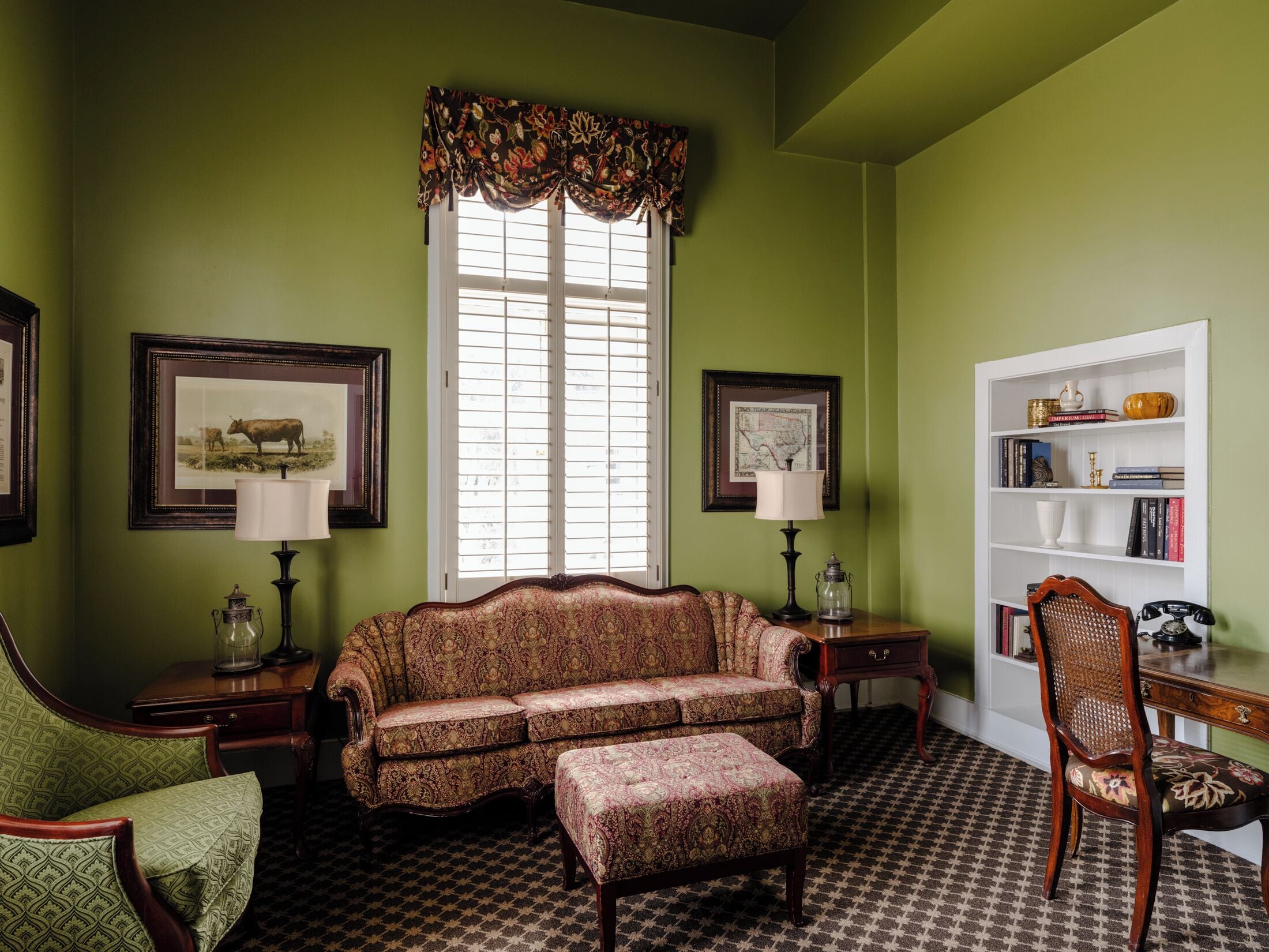 A room with a patterned floor, a sofa, a chair, a desk, and a bookshelf.