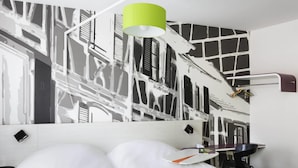 Habitación de hotel con cama, escritorio, silla, lámpara y pared decorada con un diseño abstracto en blanco y negro.