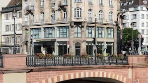 Un edificio histórico con una entrada amplia, un puente peatonal y un río.