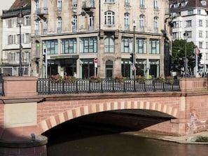 Un edificio histórico con una entrada amplia, un puente peatonal y un río.