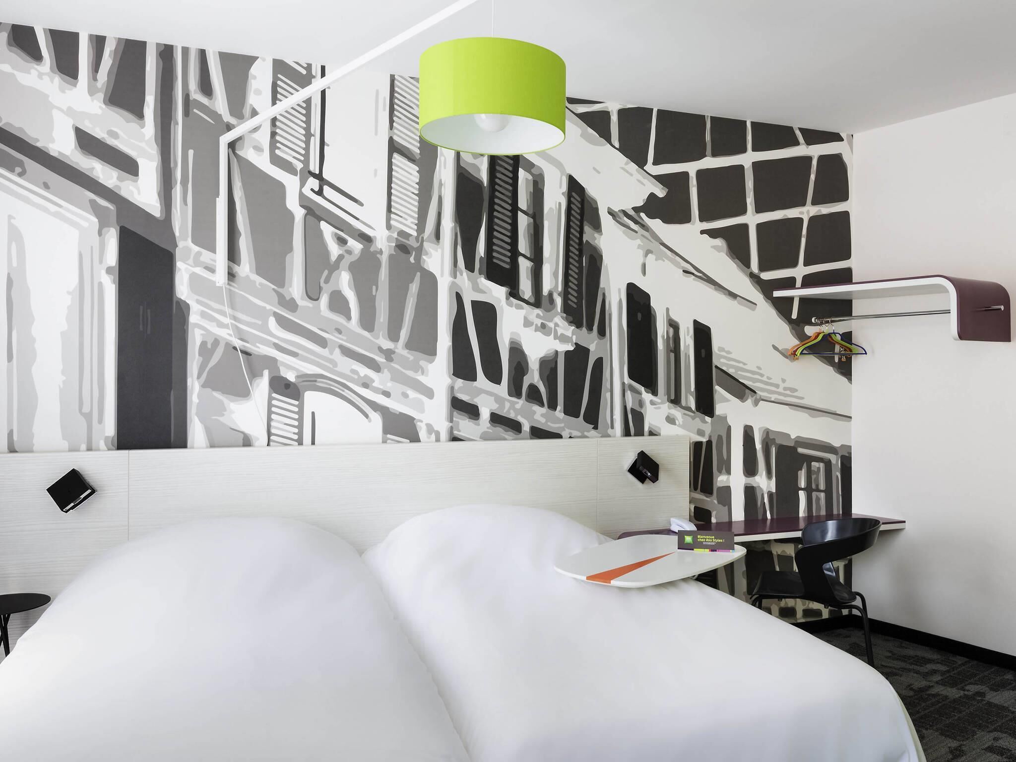 Habitación de hotel con cama, escritorio, silla, lámpara y pared con diseño abstracto en blanco y negro.