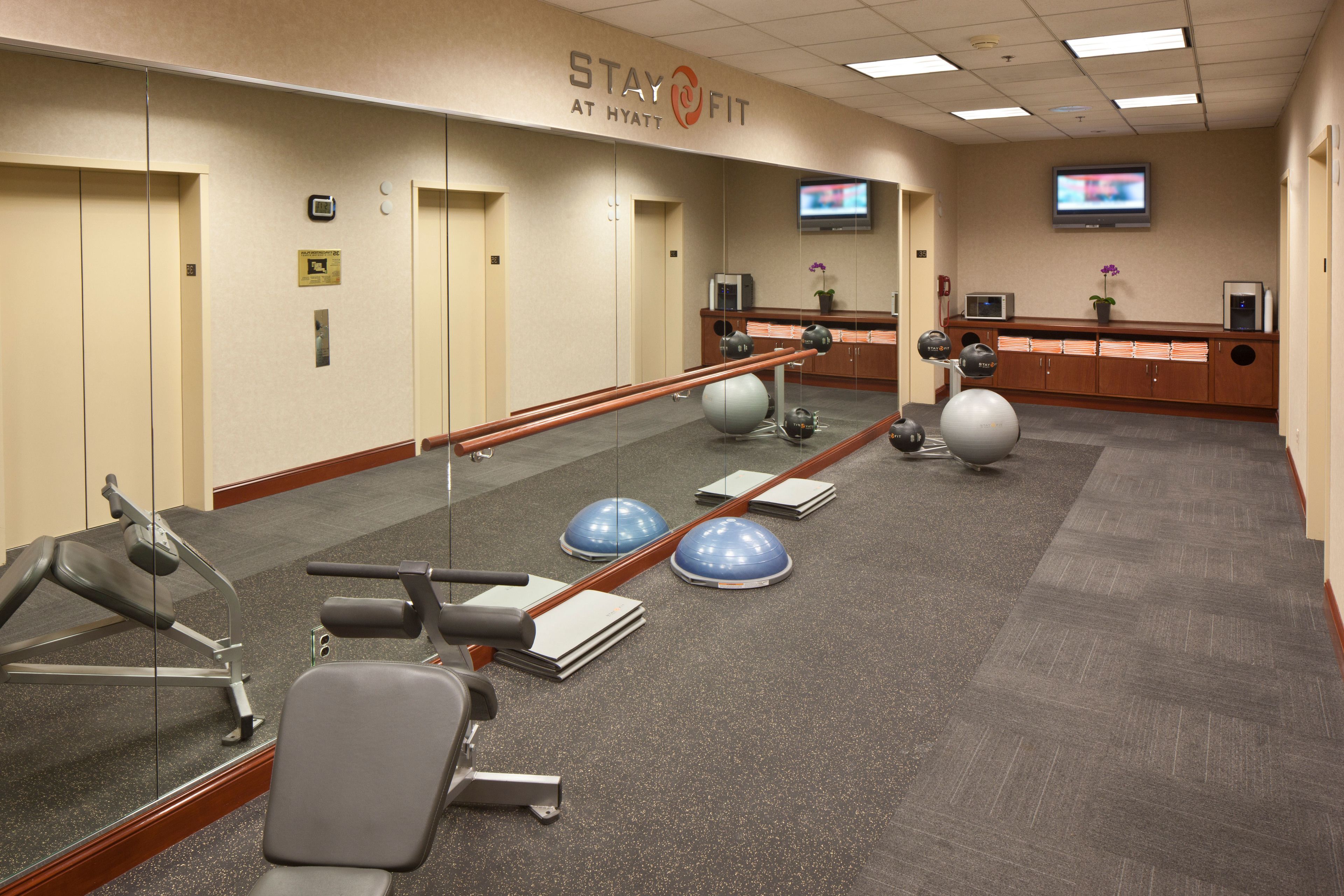 A hotel fitness center with exercise equipment, a reception desk, and a television on the wall.