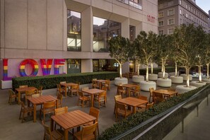 An outdoor seating area with wooden tables and chairs, a hedge, and a building with a 'LOVE' sign.