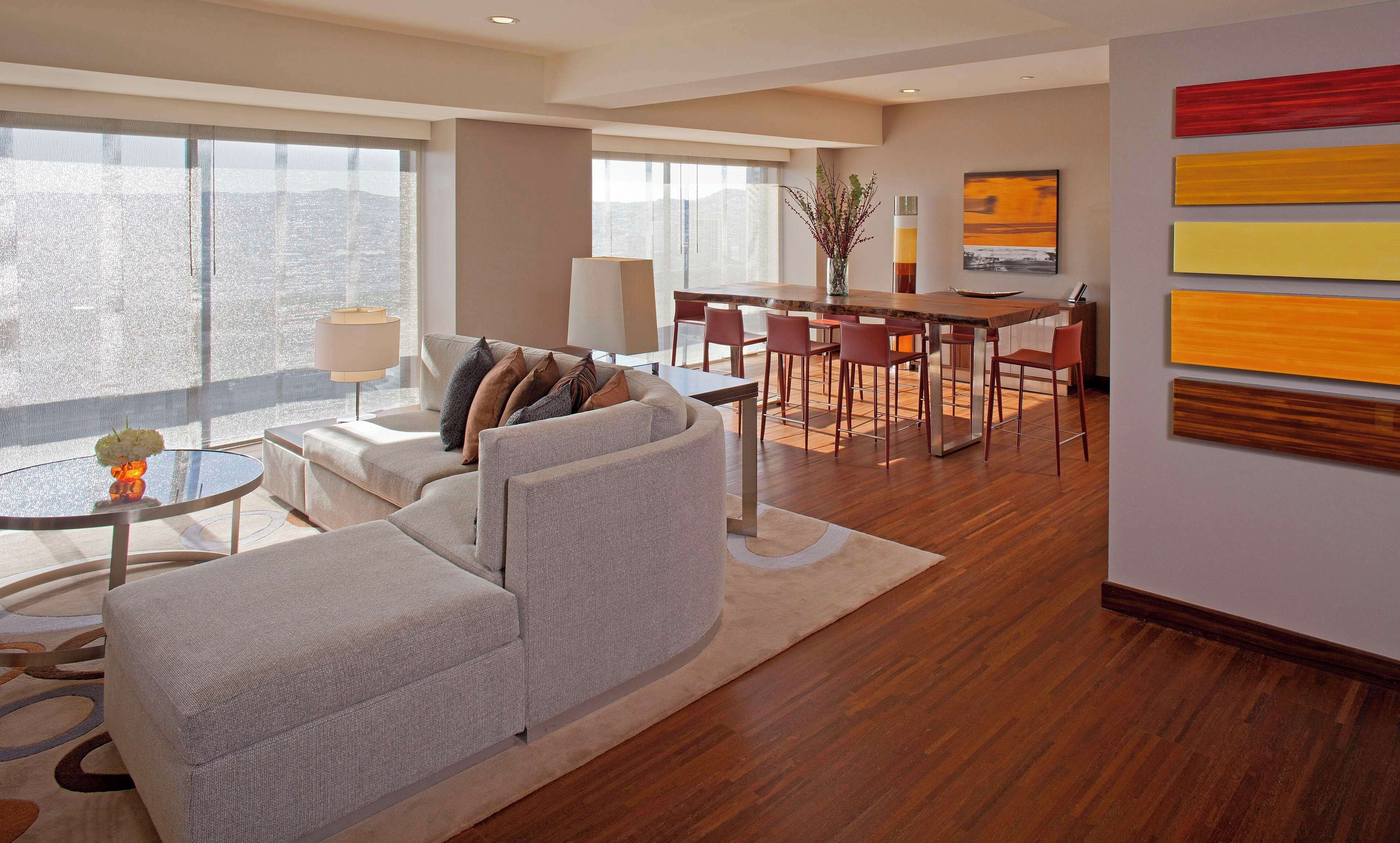 Una sala de estar moderna con un sofá, una mesa de comedor con sillas y un amplio ventanal con vista a la ciudad.
