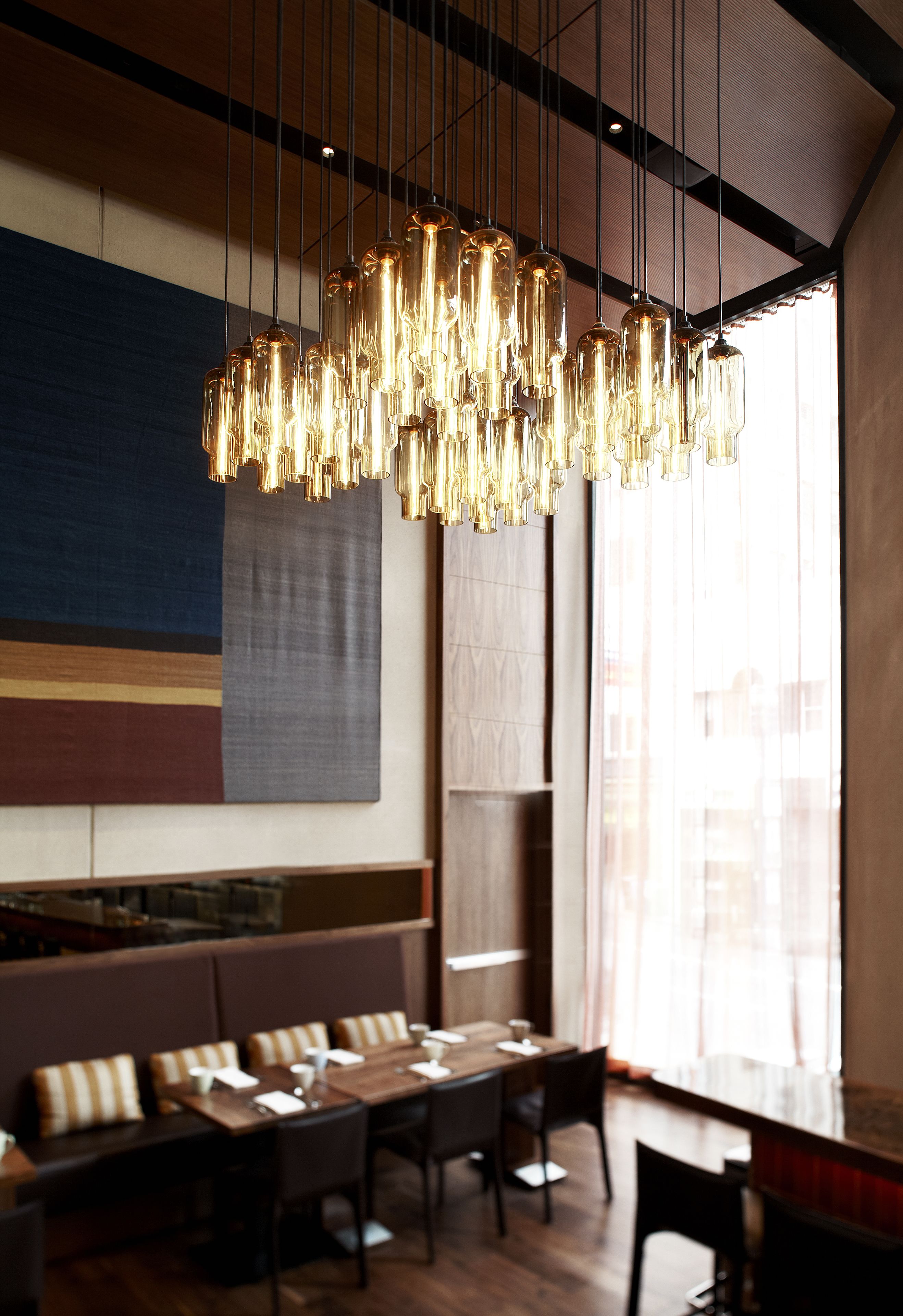 A modern restaurant interior with a long dining table, booths, and hanging light fixtures.