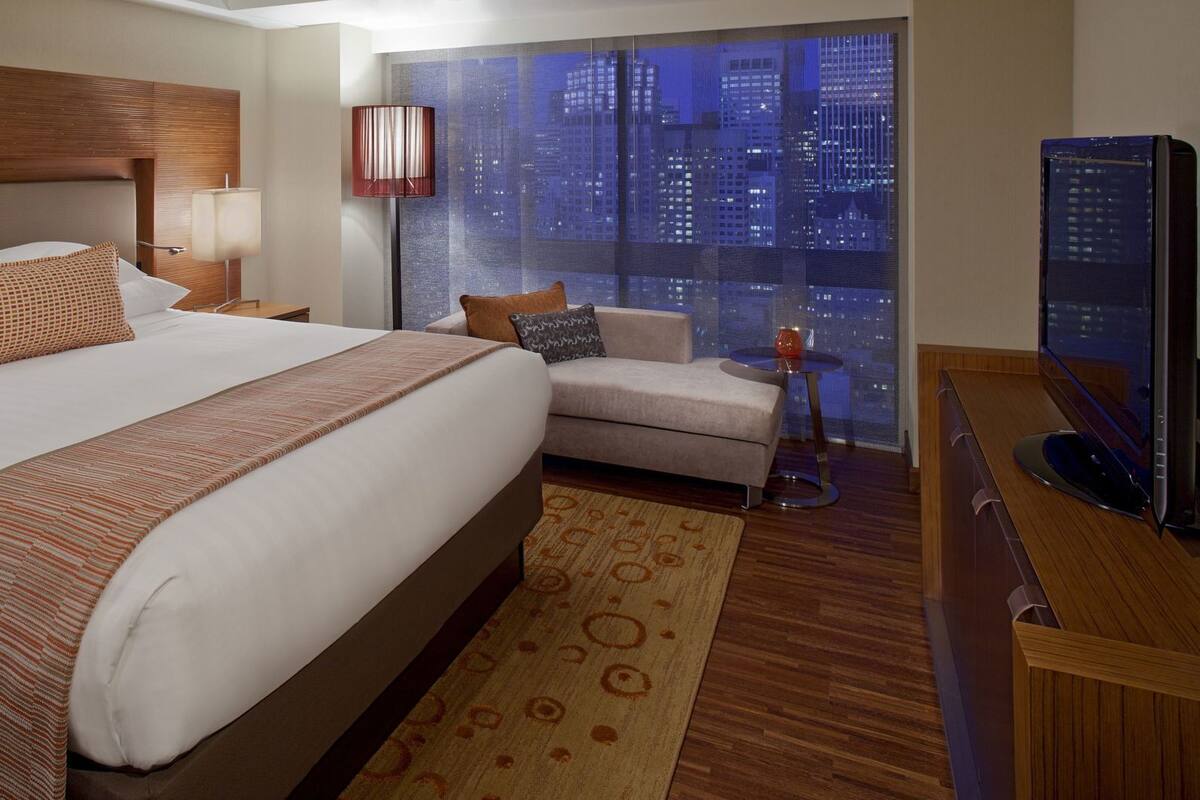 A hotel room with a large bed, a sofa, a TV, and a view of the cityscape.