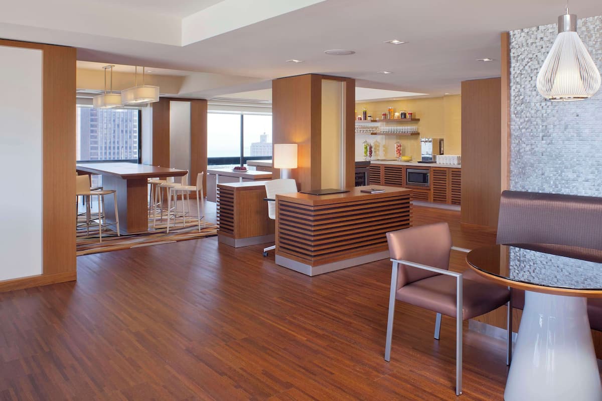 A modern hotel lobby with a wooden reception desk, seating area, and a bar with a city view.