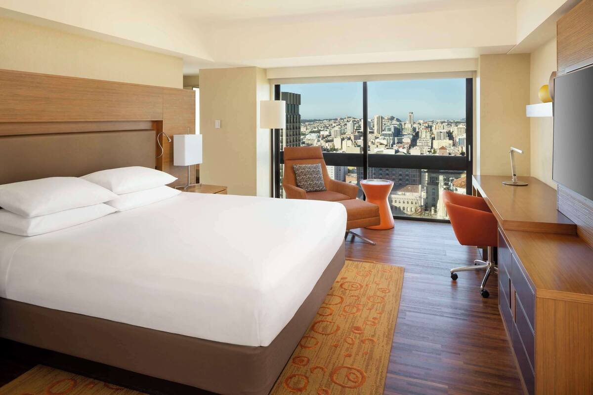 A hotel room with a large bed, a desk, a chair, and a view of the city.
