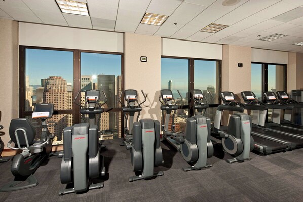 A gym with cardio machines, a treadmill, and a view of the cityscape through large windows. - Grand Hyatt San Francisco (San Francisco)