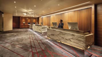 A modern hotel reception area with marble counters, wooden paneling, and a geometric patterned carpet.
