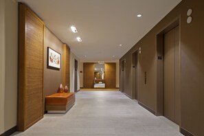 A modern hotel corridor with wooden paneling, a bench, and a framed artwork.