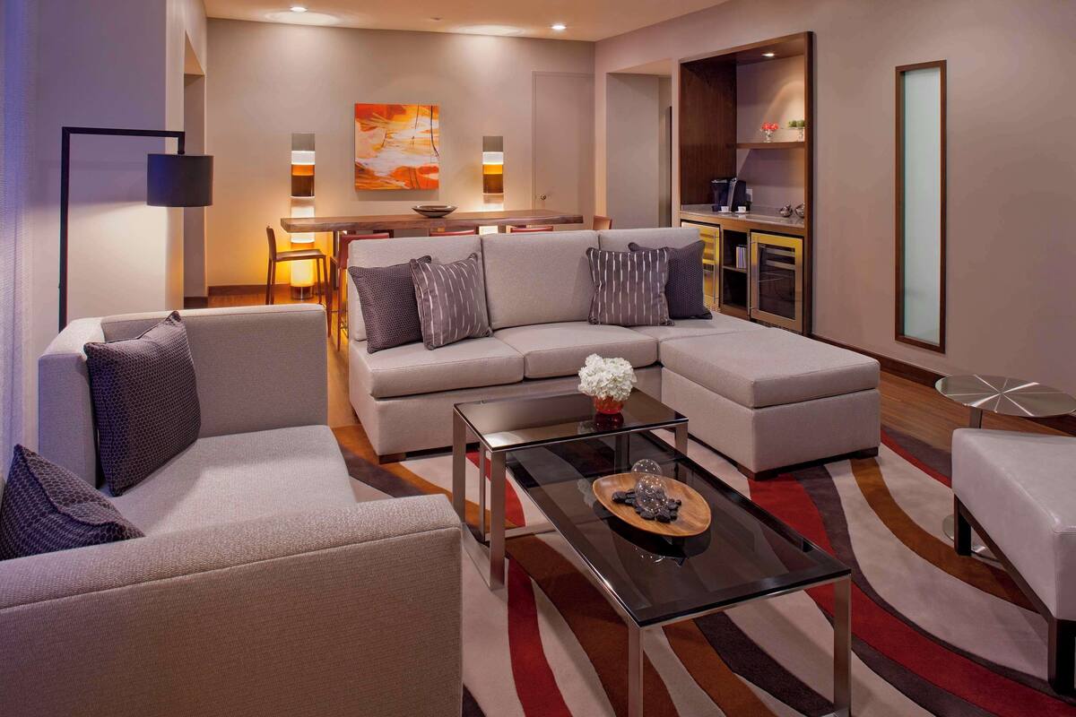 A modern living room with a sofa, armchairs, a coffee table, and a dining area with a kitchen in the background.