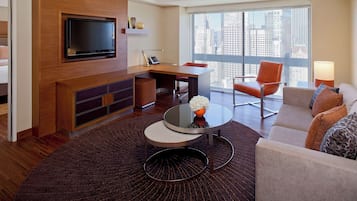 A modern living room with a flat-screen TV, a desk, a round coffee table, and a sofa with decorative pillows.